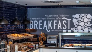 A breakfast buffet area with various food items, a wall with a quote, and hanging lights. - Premier Inn München City Schwabing (Munich)