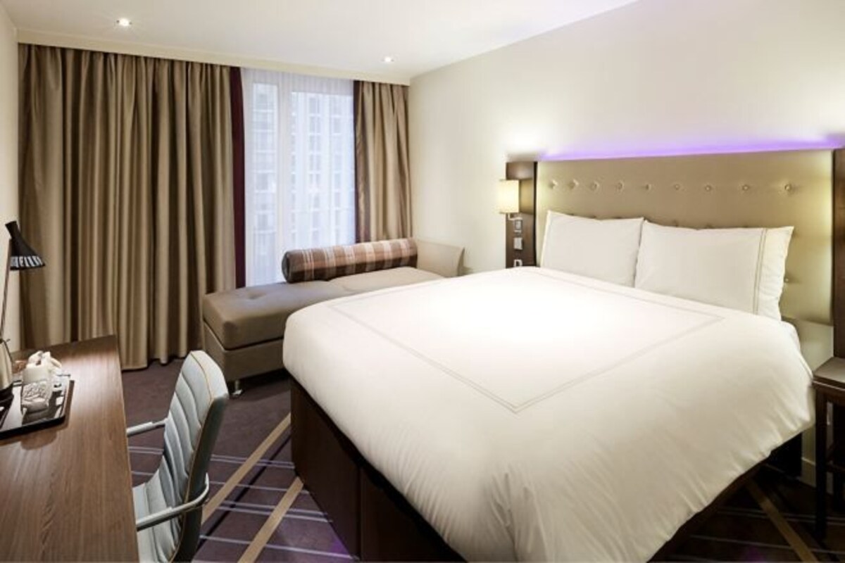 A hotel room with a large bed, a desk, a chair, a small sofa, and a window with curtains.