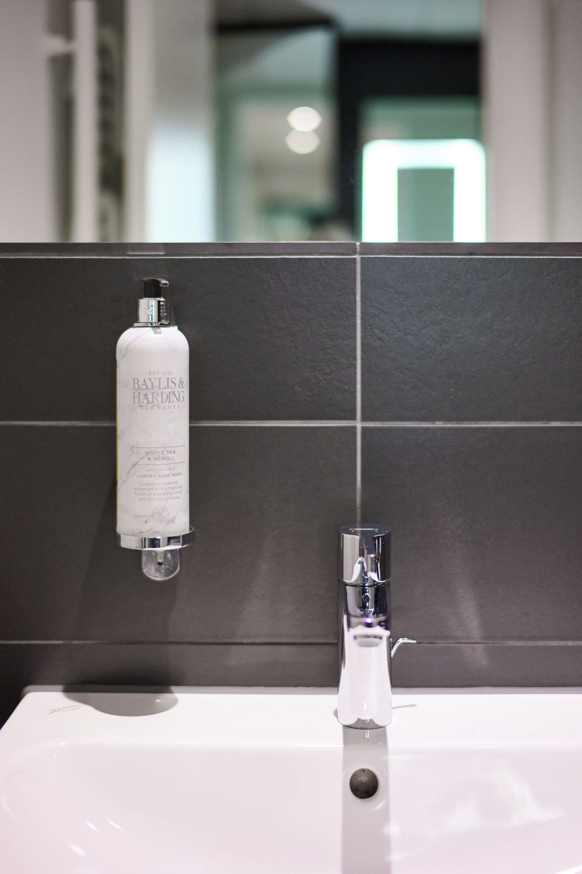 A bathroom with a white sink, a bottle of Baylis & Harding white tea, and a glass faucet.