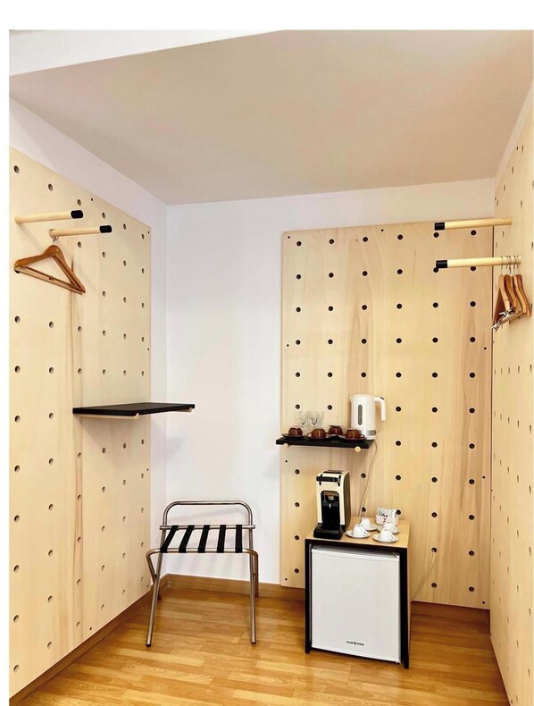 A compact room with a bed, a small table with a coffee machine, and a wardrobe with hanging clothes. - Hotel Imago (Bari)