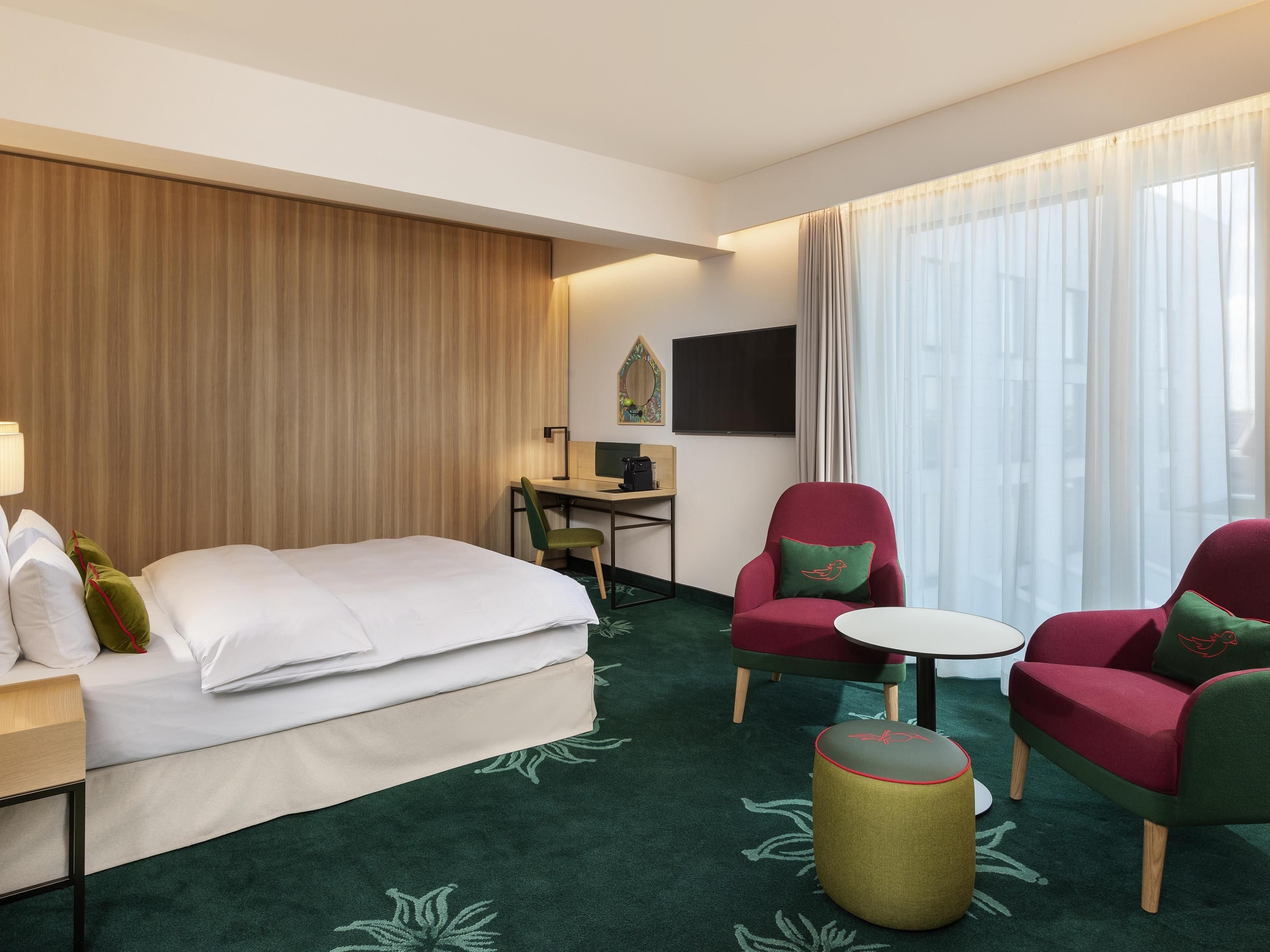 Habitación de hotel con una cama, dos sillones, un escritorio con una computadora y una mesita redonda.