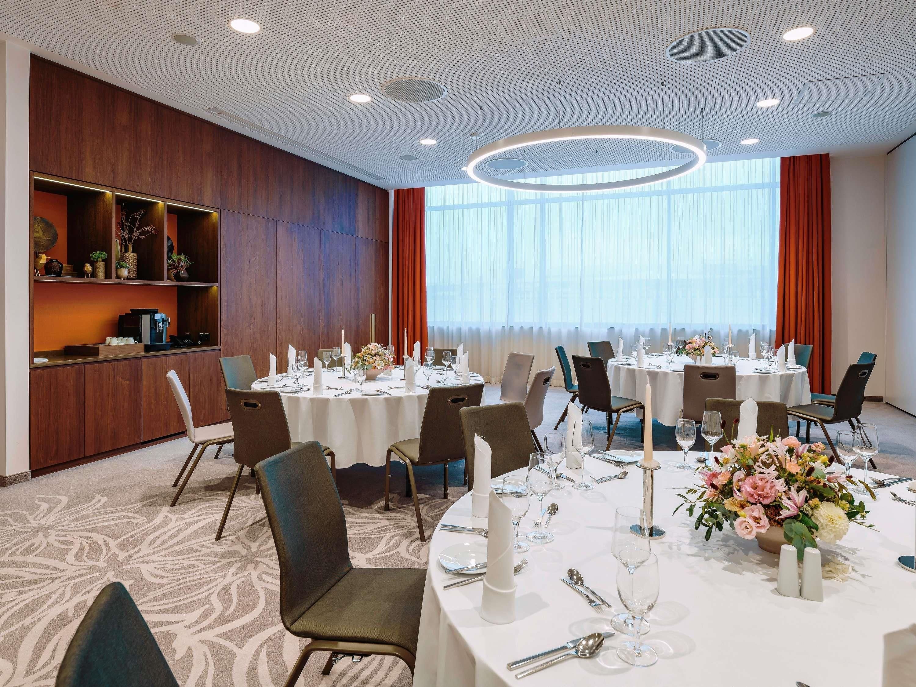 A hotel dining area with round tables, chairs, and a bar area with shelves.