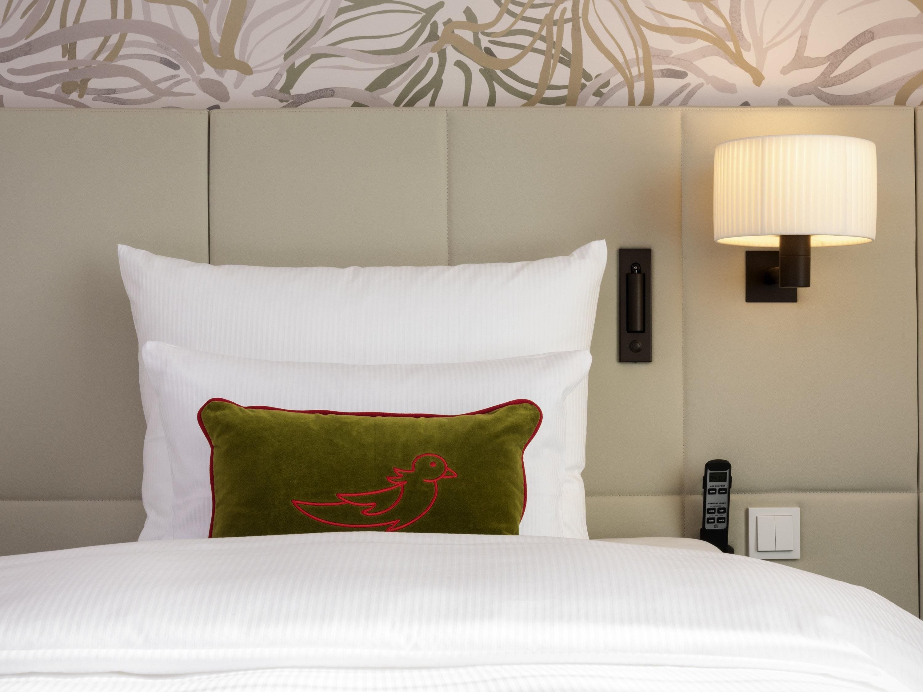 A neatly made bed with white and green pillows, a wall-mounted lamp, and a telephone on the side.