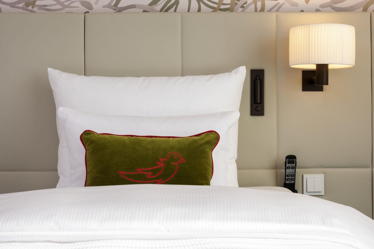 A neatly made bed with white and green pillows, a wall-mounted lamp, and a telephone on the side.