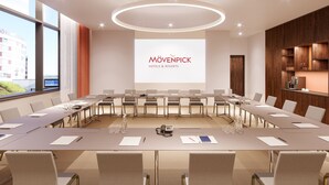 Un salón de conferencias con una larga mesa, sillas, una pantalla de proyector mostrando