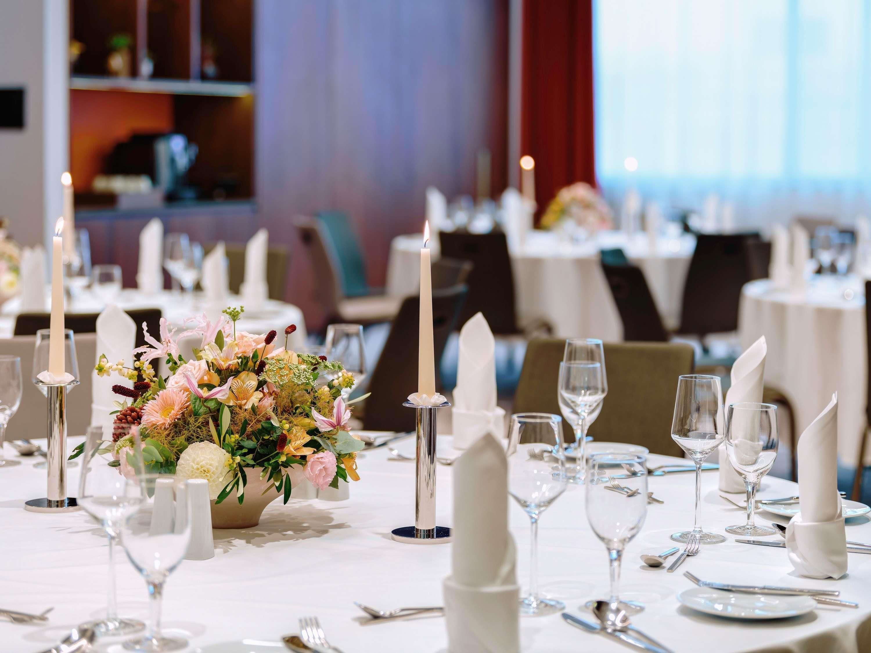 Un comedor con mesas dispuestas para una comida, velas y un centro de mesa floral.