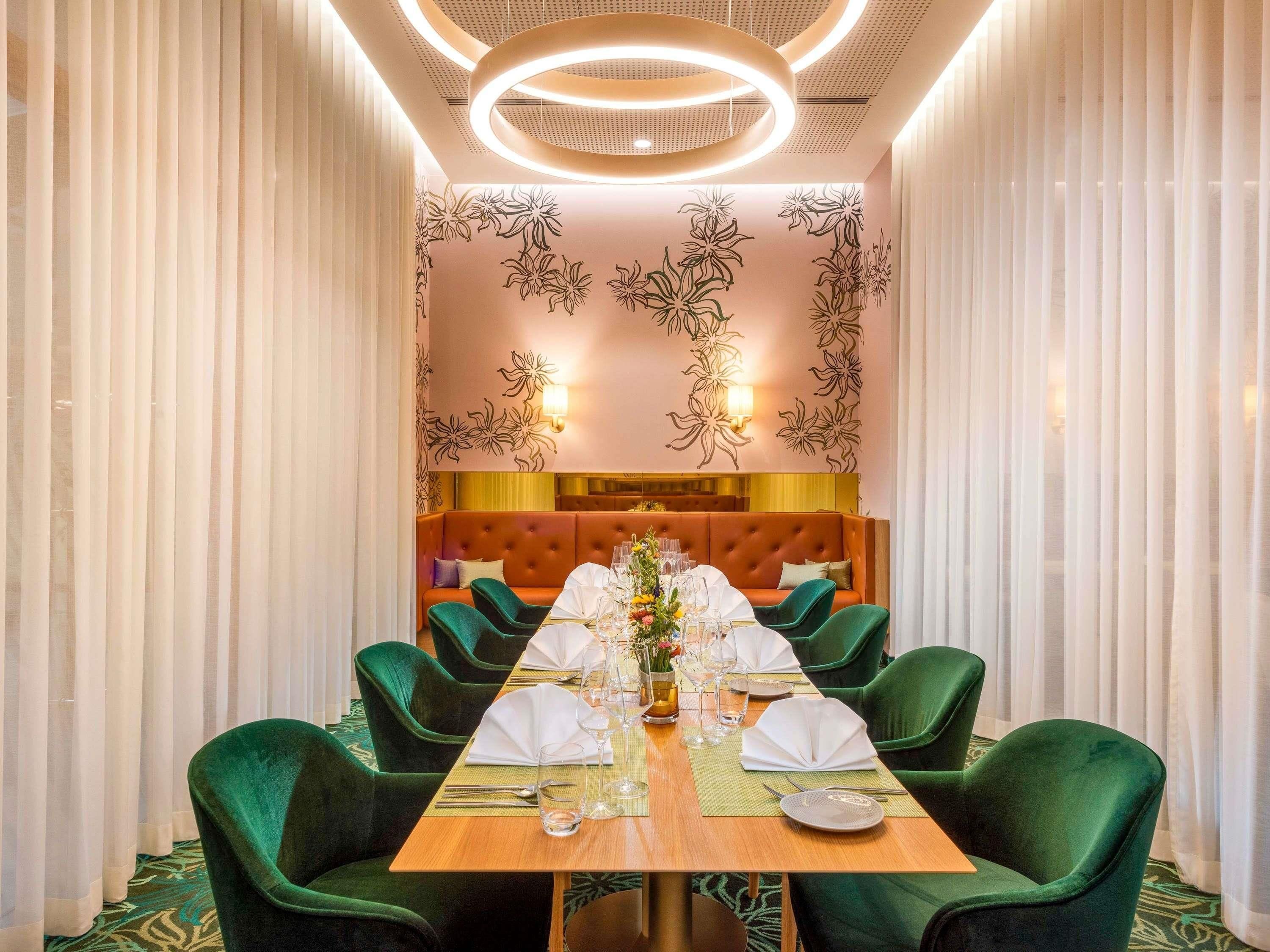 A dining area with a long table set for six, surrounded by green upholstered chairs.