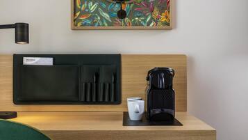 A neatly arranged hotel room with a wooden headboard, a black leather wallet with pens, a white mug, and a black coffee maker on a wooden table.