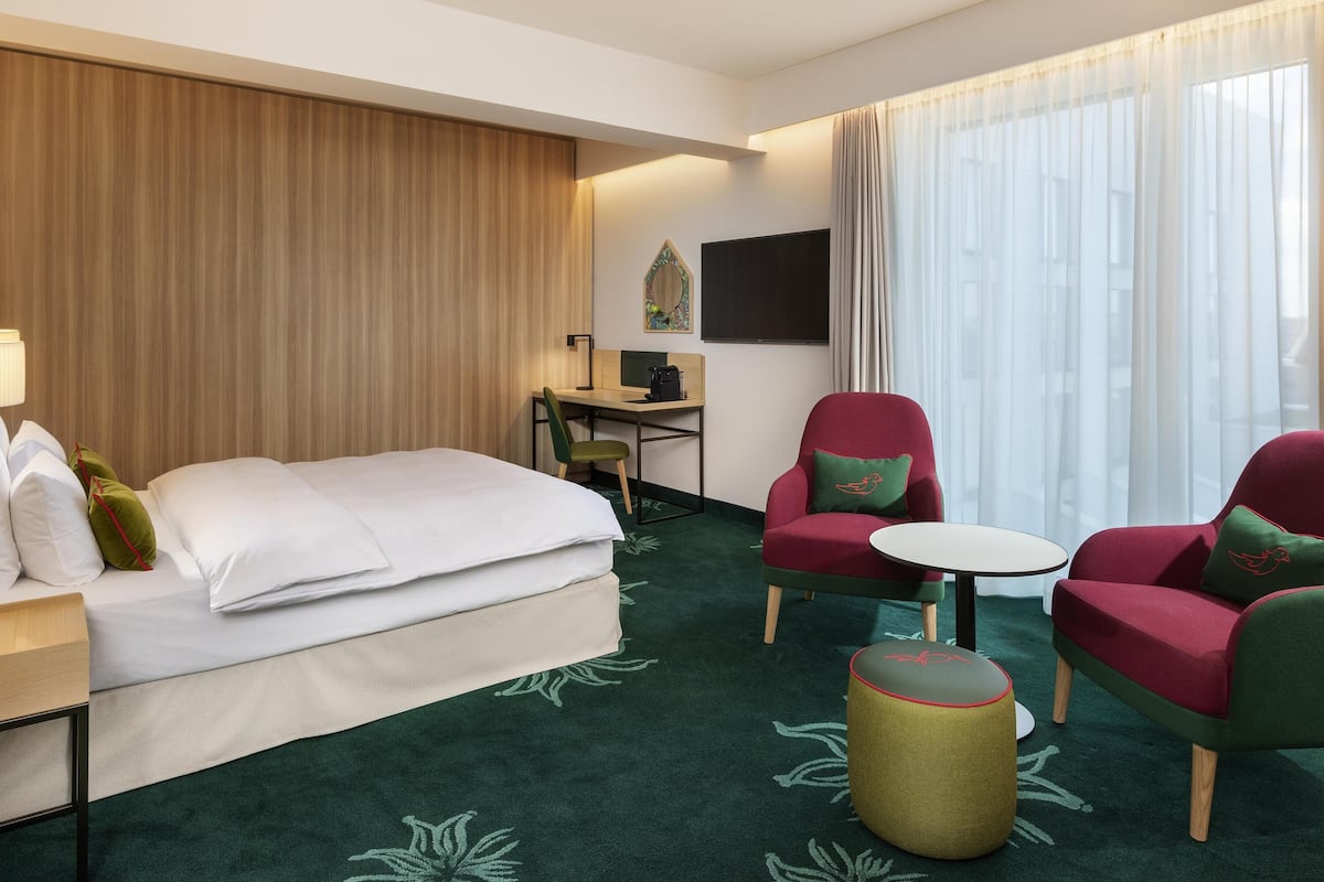 Ett hotellrum med en säng, två fåtöljer, ett skrivbord med en dator och ett litet runt bord.