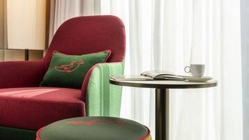 Un sillón rojo con un cojín verde y un otoman a juego, una taza blanca y un libro sobre una mesita redonda.