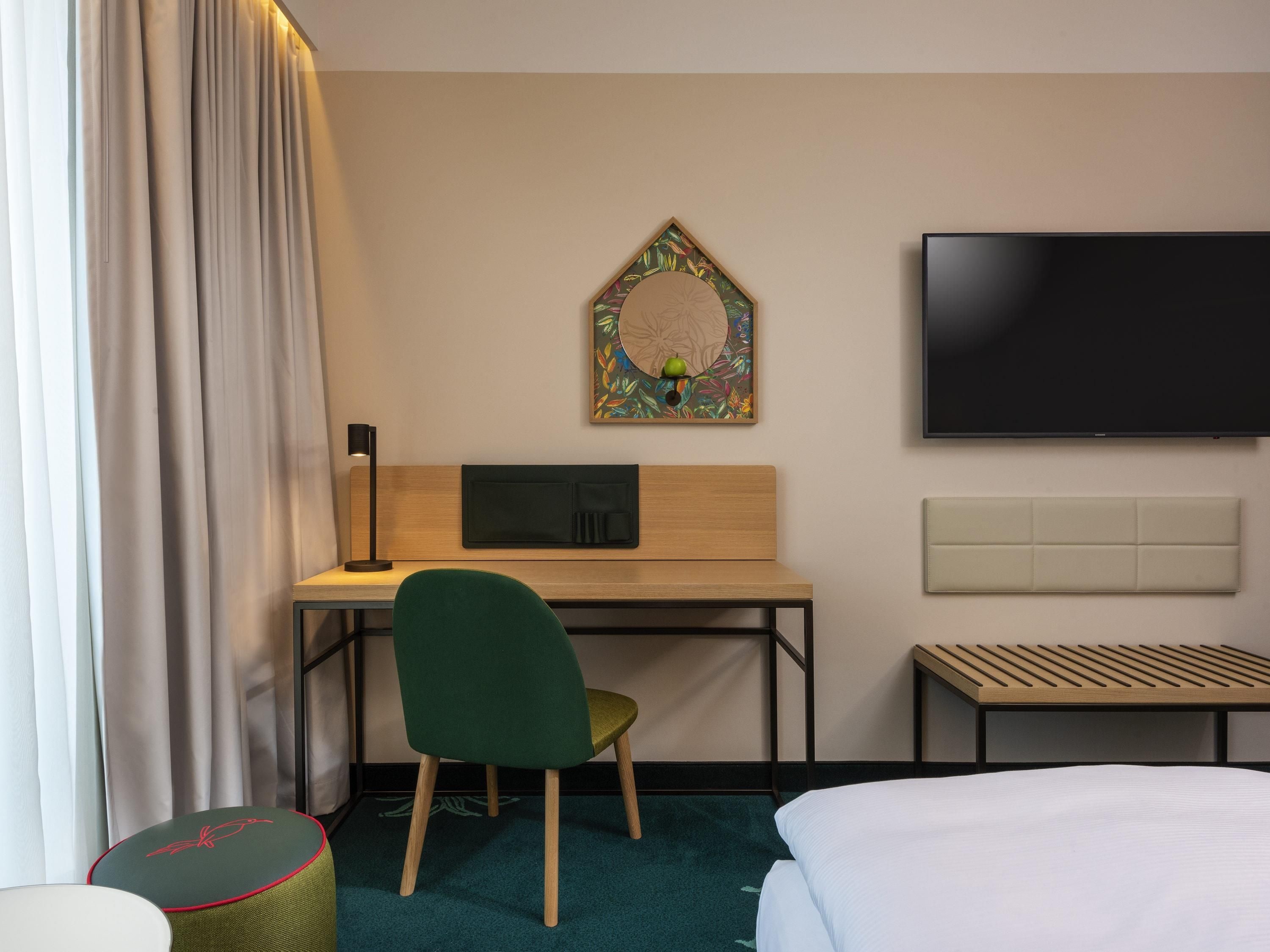 Habitación de hotel con cama, escritorio con silla, televisor y una obra de arte colgada en la pared.