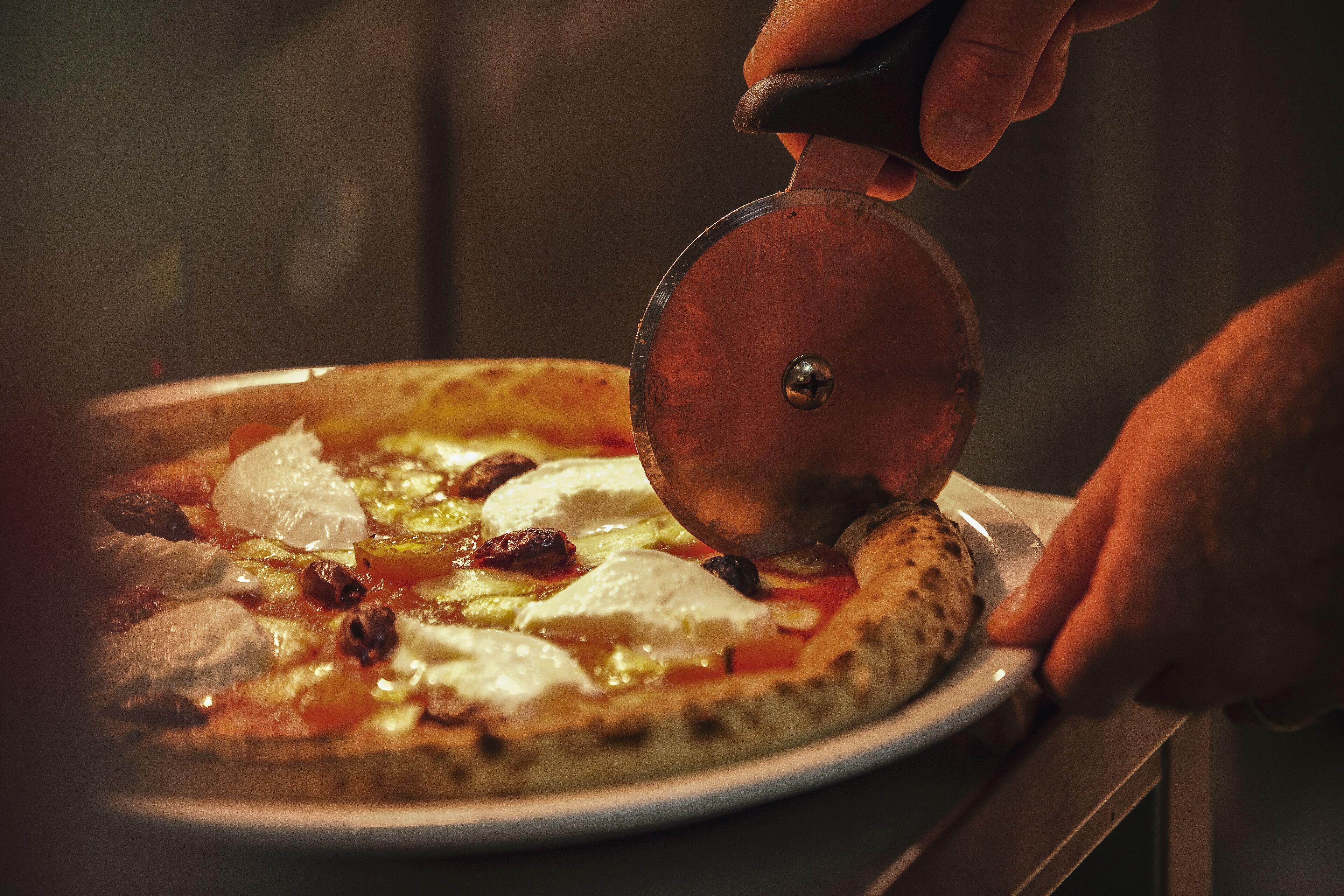Pizza sendo cortada com um cortador de pizza.