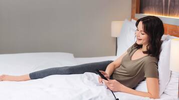Une personne allongée sur un lit, avec un oreiller blanc et une couverture noire, tenant un téléphone intelligent.