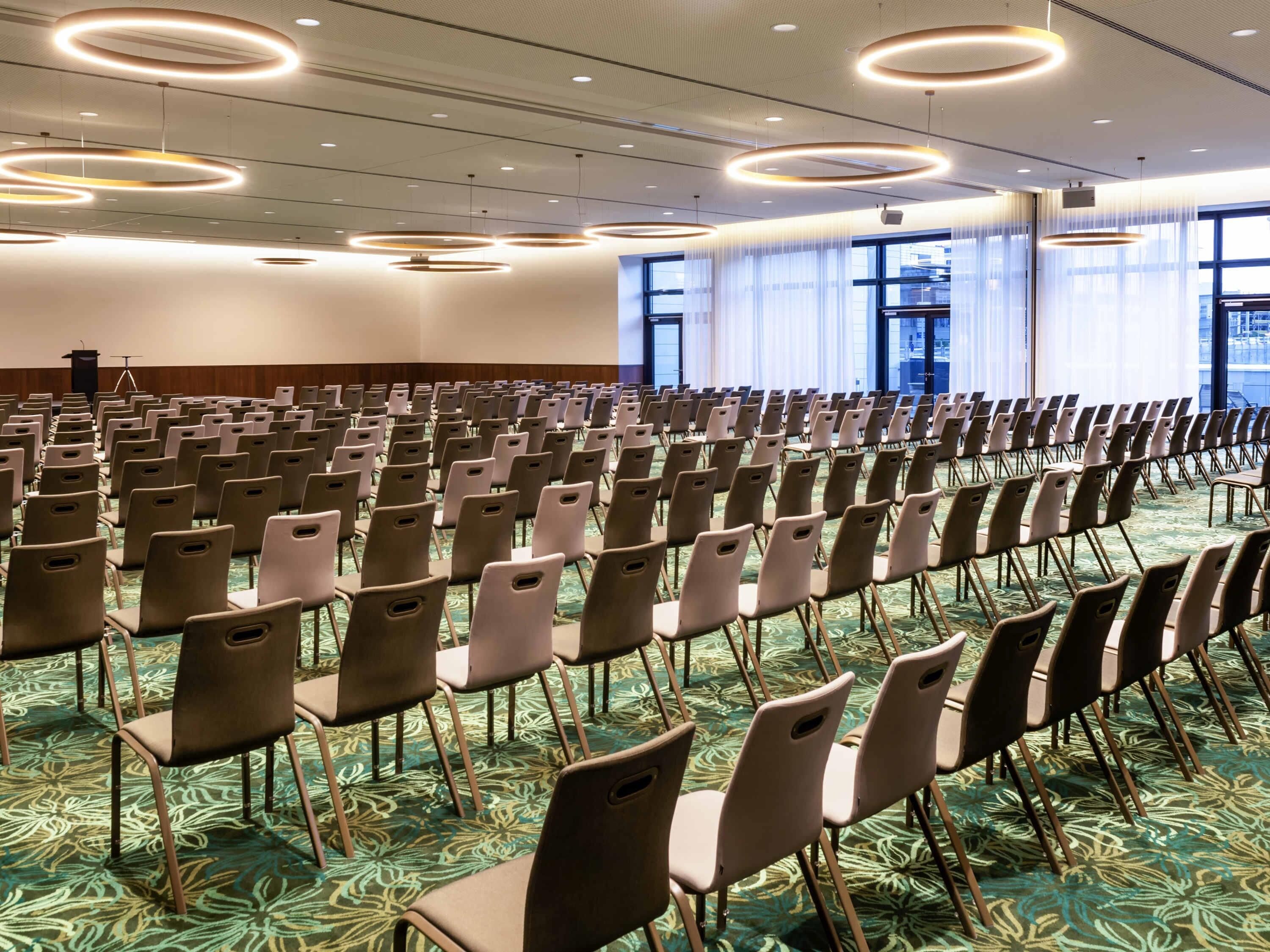 Un salón de conferencias con filas de sillas, un atril y grandes ventanales.