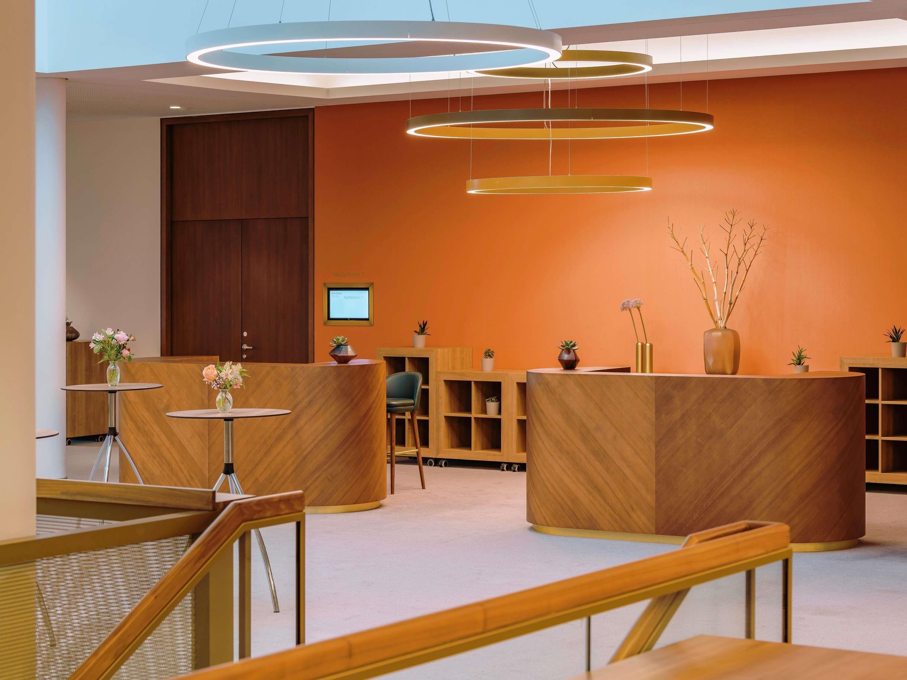 A modern reception area with wooden reception desks, a digital screen, and a staircase.