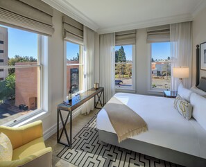 A hotel room with a large bed, a desk with a lamp, a chair, and a view of the city.