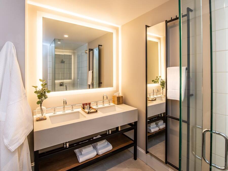 A modern bathroom with a large mirror, dual sinks, and a glass-enclosed shower.