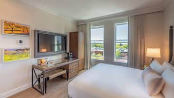 A hotel room with a bed, TV, desk, and a balcony with a view.