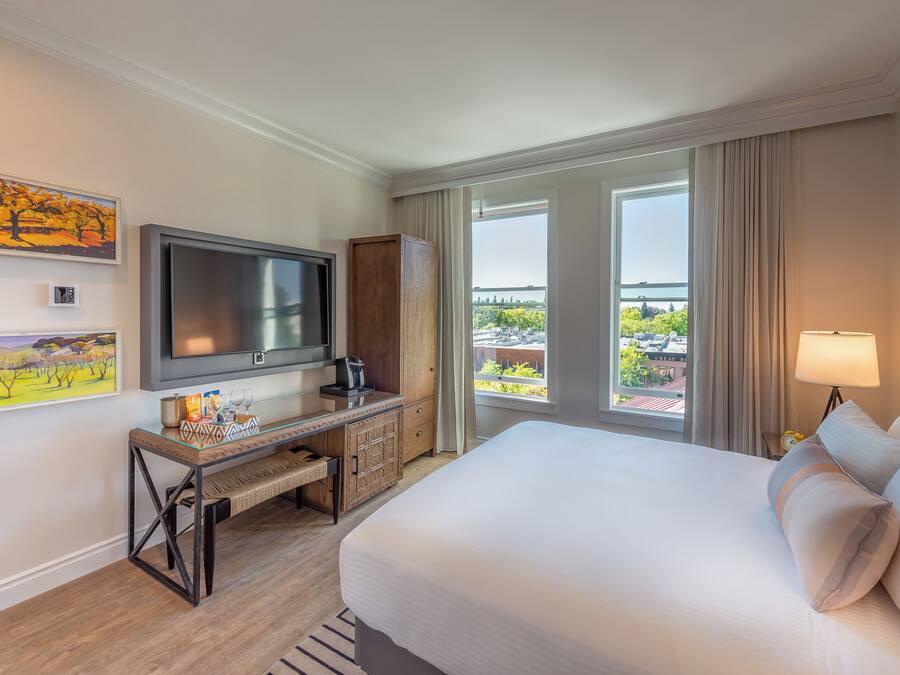 A hotel room with a bed, TV, desk, and a balcony with a view.