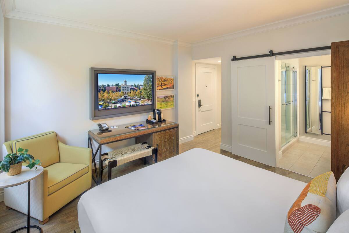 A hotel room with a bed, a desk with a computer, a television, a chair, and a wardrobe.