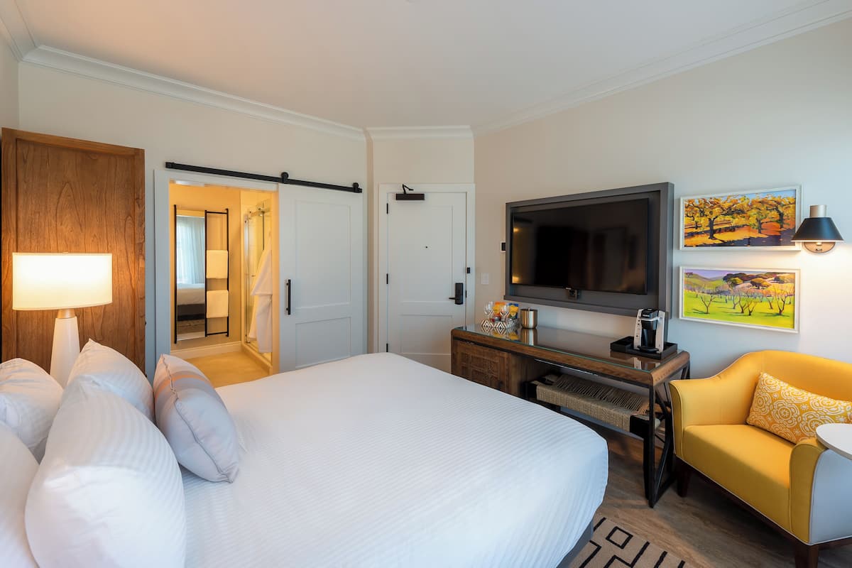 A hotel room with a bed, a TV, a sofa, and a painting on the wall.