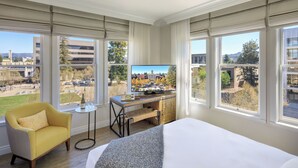 A hotel room with a bed, a desk, a chair, a TV, and large windows offering a city view. - Hotel E (Santa Rosa)