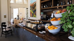 A breakfast bar with bowls of fruit, a coffee machine, and a wine rack in the background. - Hotel E (Santa Rosa)