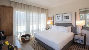 A hotel room with a large bed, a wooden desk with a bottle of champagne, a small bucket, and a nightstand with a lamp.
