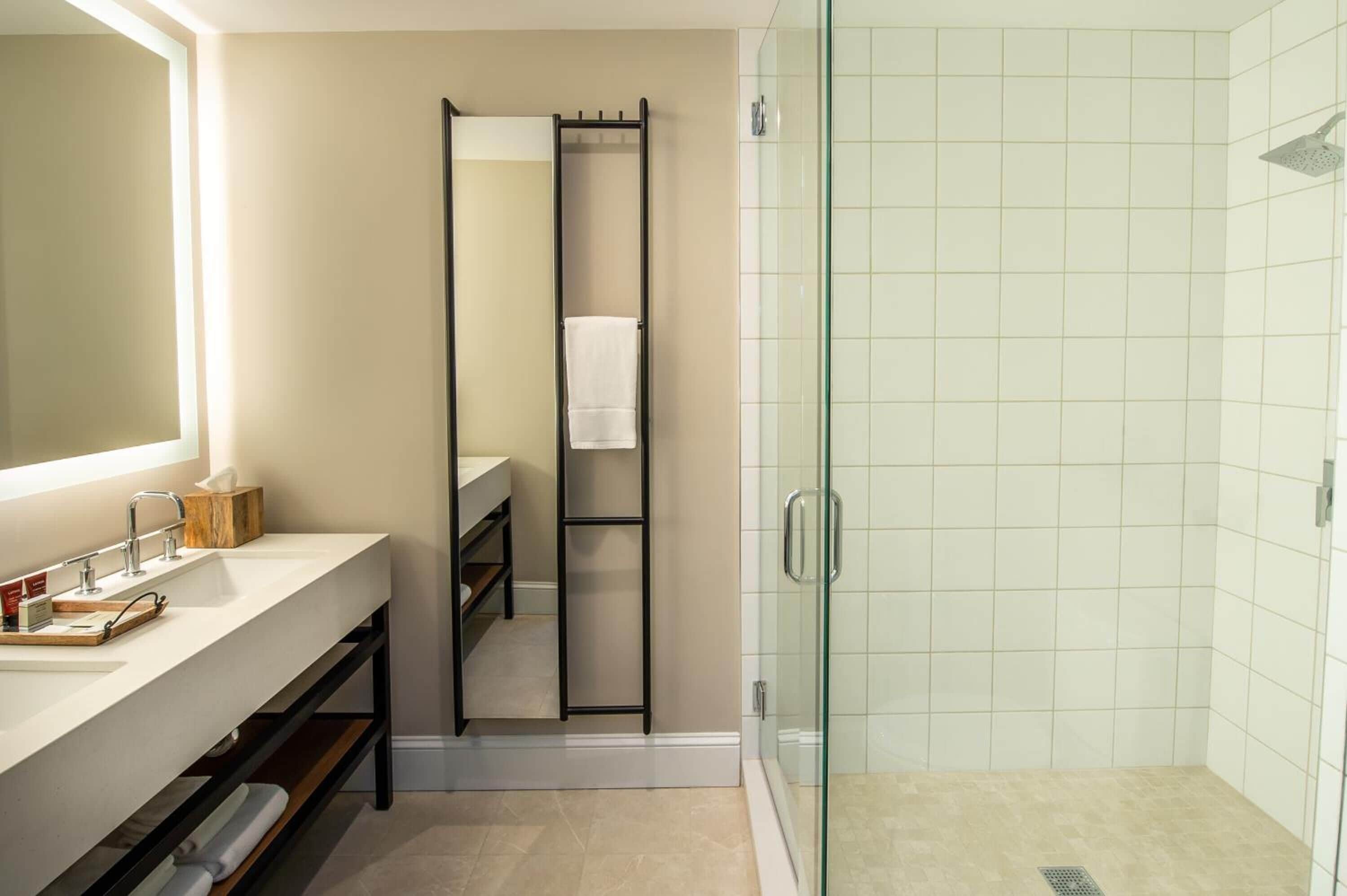 A modern bathroom with a large mirror, a glass-enclosed shower, and a vanity with a sink and shelves.