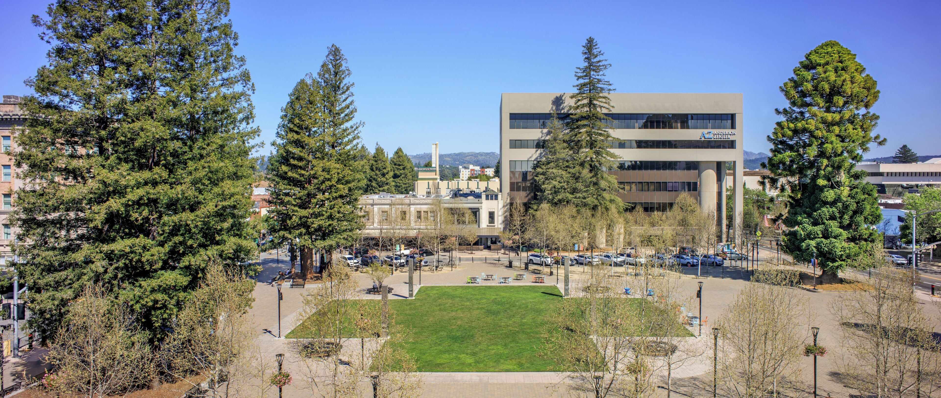 A campus with a central lawn, modern buildings, and a parking area.