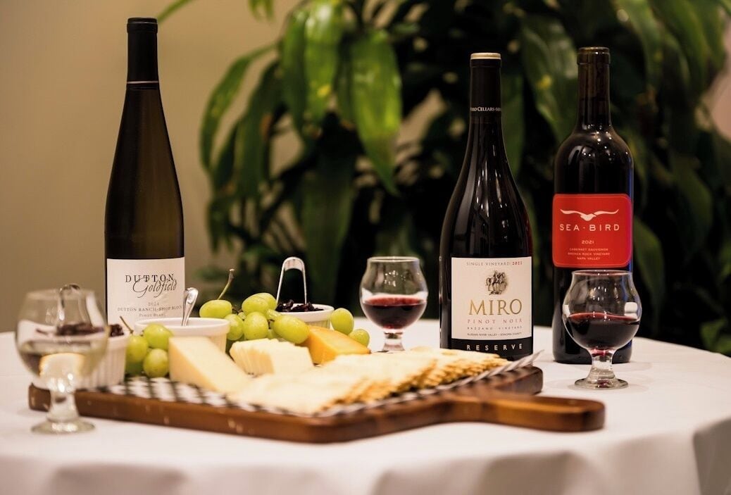 A table with three wine bottles, a cheese board with various cheeses, grapes, and a glass of red wine.