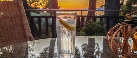 Un vaso de agua sobre una mesa, con vistas a árboles y una puesta de sol al fondo.