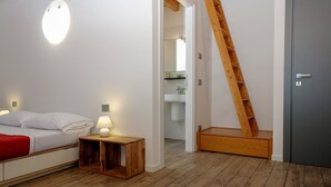 Een slaapkamer met een bed, nachtkastje en een houten ladder naar een badkamer.