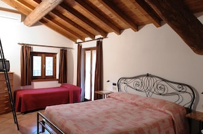 Quarto com duas camas de solteiro, vigas de madeira no teto, uma janela com cortinas e uma mesa de cabeceira.