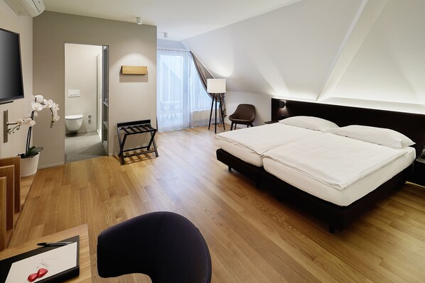 Una habitación de hotel moderna con una cama grande, un escritorio con una silla, una mesita y un televisor.