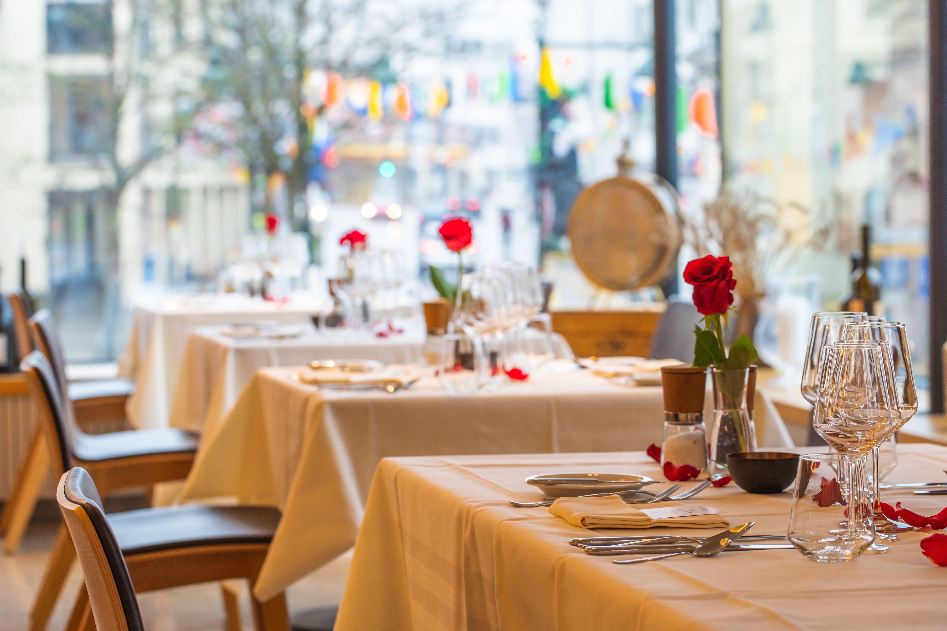 Ein Restaurant mit gedeckten Tischen, ausgestattet mit klarem Glas und roten Rosen als Dekoration.