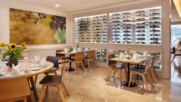 A restaurant with multiple tables and chairs, a large wine display, and a painting on the wall.
