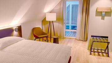 A hotel room with a bed, a chair, a lamp, a small table, and a view of the outside.