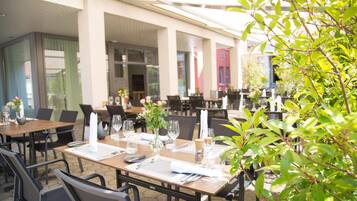 An outdoor dining area with tables set for two, featuring white napkins, wine glasses, and cutlery.