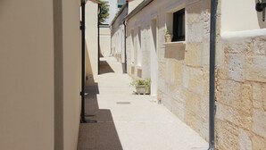 Une ruelle étroite aux murs de pierre et au sol carrelé, qui mène à un bâtiment doté de nombreuses fenêtres et d’une porte.