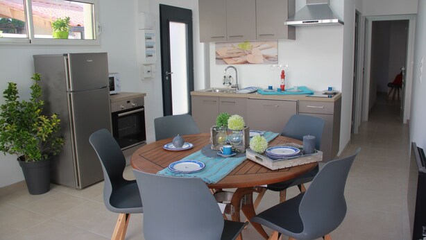 Une cuisine moderne équipée d’un four encastré, d’un réfrigérateur et d’un coin repas avec une table en bois et quatre chaises.