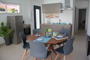 Une cuisine moderne équipée d’un four encastré, d’un réfrigérateur et d’un coin repas avec une table en bois et quatre chaises.