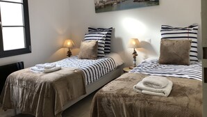 Une chambre d’hôtel avec deux lits, une literie à rayures et un tableau représentant une ville côtière.