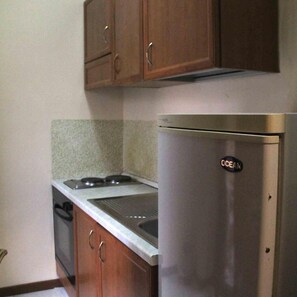 A compact kitchen with a stainless steel refrigerator, a stove, and wooden cabinets. - Hotel Cristal (Bari)