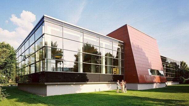 Un bâtiment moderne doté de grandes fenêtres en verre et d’une façade distinctive aux couleurs rouge et blanche.