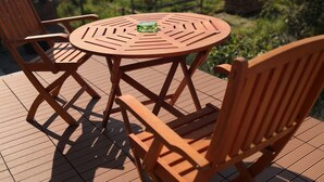 Une terrasse extérieure en bois, avec une table ronde et quatre chaises, entourée d’un jardin et d’immeubles résidentiels.