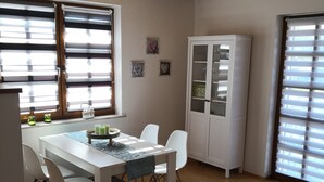 Un coin repas avec une table et des chaises blanches, un buffet avec des portes en verre et un plafond orné de poutres en bois.