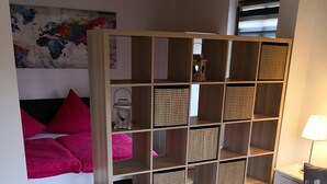 Un salon moderne avec un plancher en bois, une table basse blanche ornée de bougies, un canapé noir et une grande bibliothèque en bois.