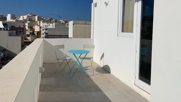 A balcony with a table and chairs, a sliding glass door, and a view of a densely packed urban area.