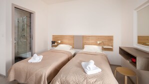 A hotel room with two beds, a shower, a desk, and a mirror. - Island Guesthouse (Gzira)